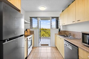 A modern kitchen with stainless steel appliances, wooden cabinets, and a view through the open door. - Coastal Retreat Moffat Beach (Moffat Beach)