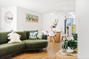 A modern living room with a green sofa, a dining area with a wooden table and chairs, and a ceiling fan. - Coastal Retreat Moffat Beach (Moffat Beach)