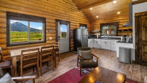 Eine Blockhütte mit Essbereich, Küche und einem großen Fenster mit Blick auf die Berge.