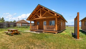Eine Holzhütte mit Veranda, Picknicktisch und einem eingezäunten Garten.