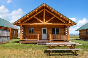 A wooden cabin with a front porch, a door, and windows.