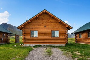 Une cabane en rondins avec un toit en pente, deux fenêtres et un chemin de gravier menant à l’entrée.