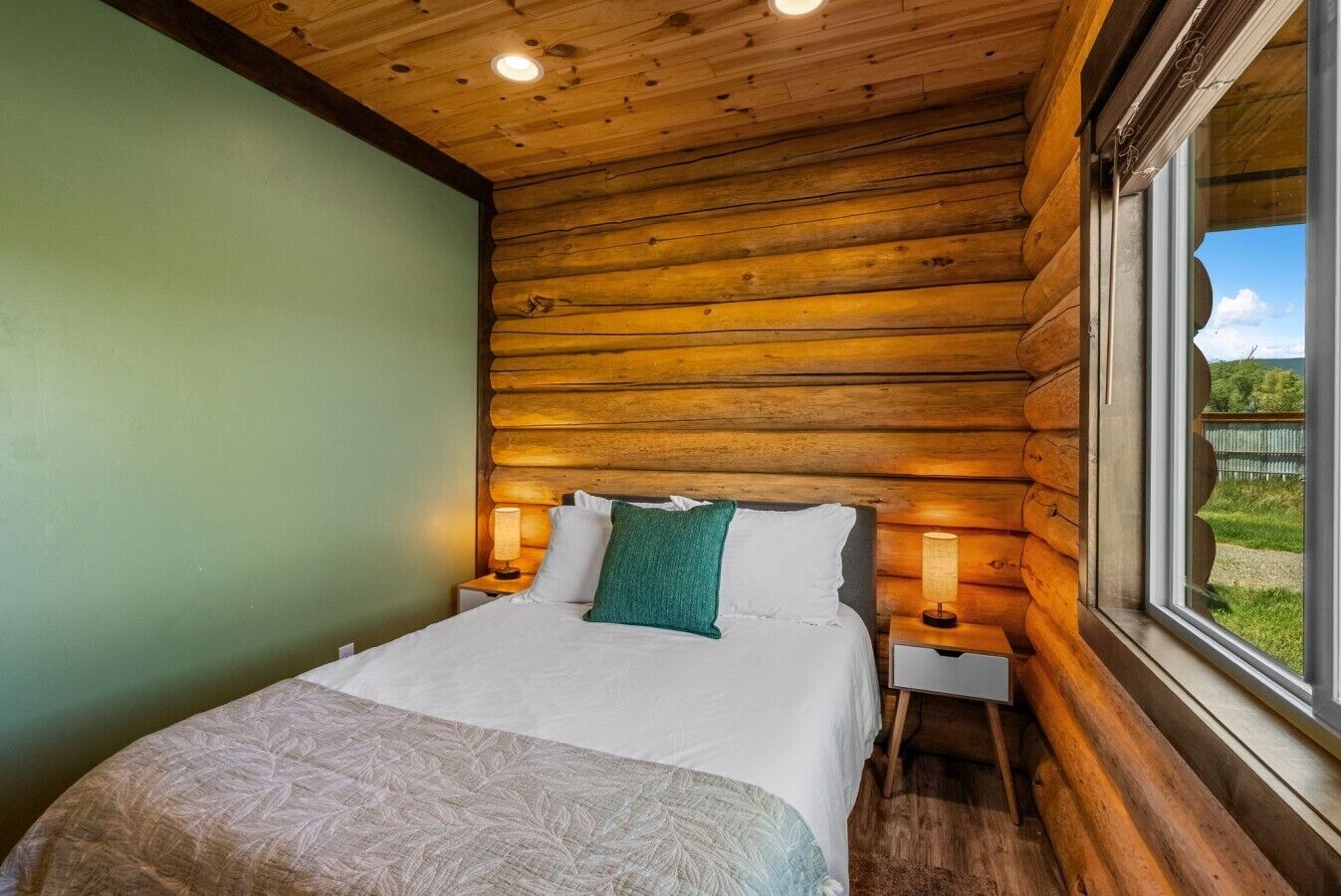 Un dormitorio tipo cabaña de madera con una cama, dos lámparas de noche y un ventanal con vistas al exterior.