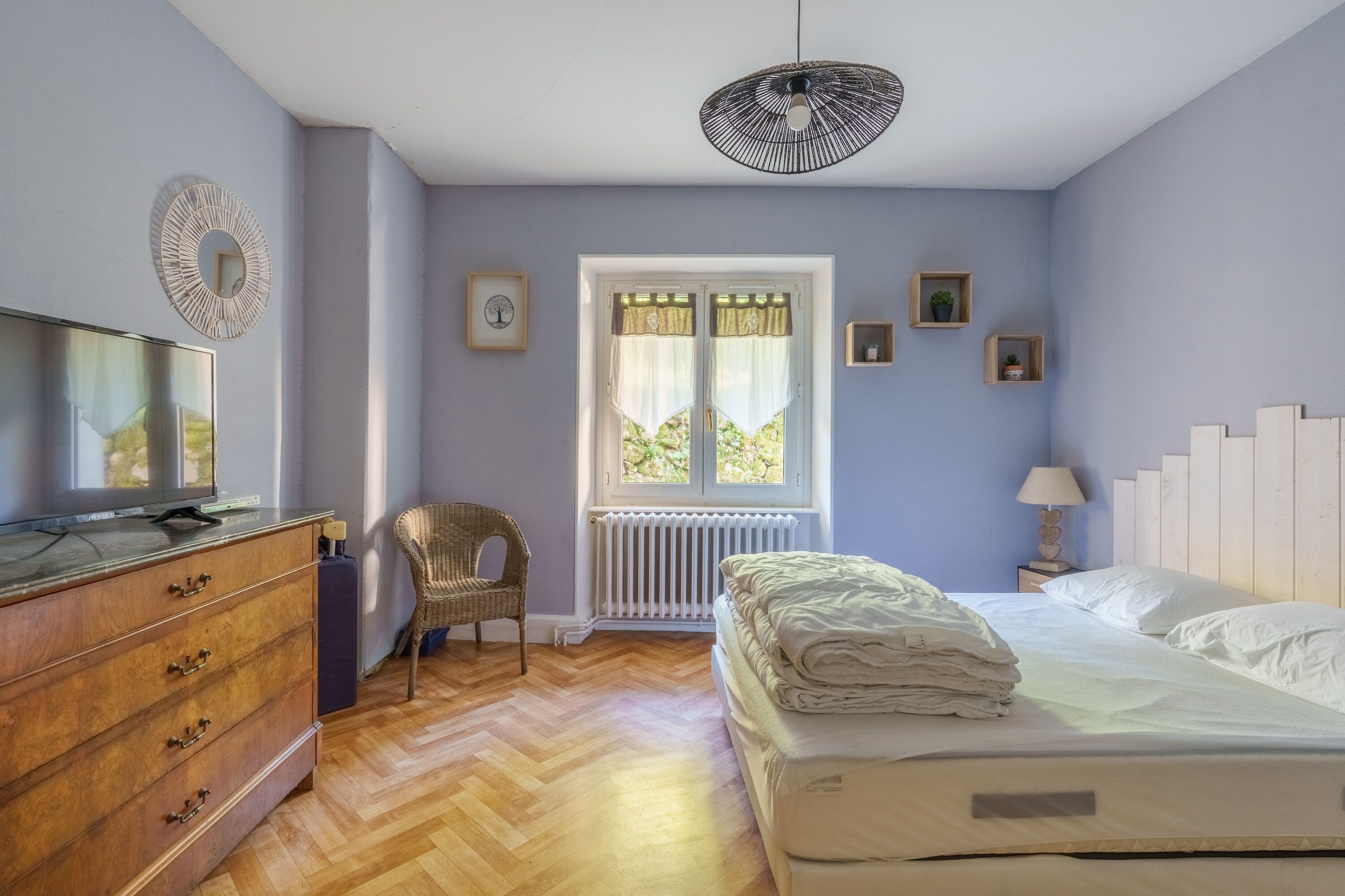 A bedroom with a bed, dresser, chair, and a window with curtains.