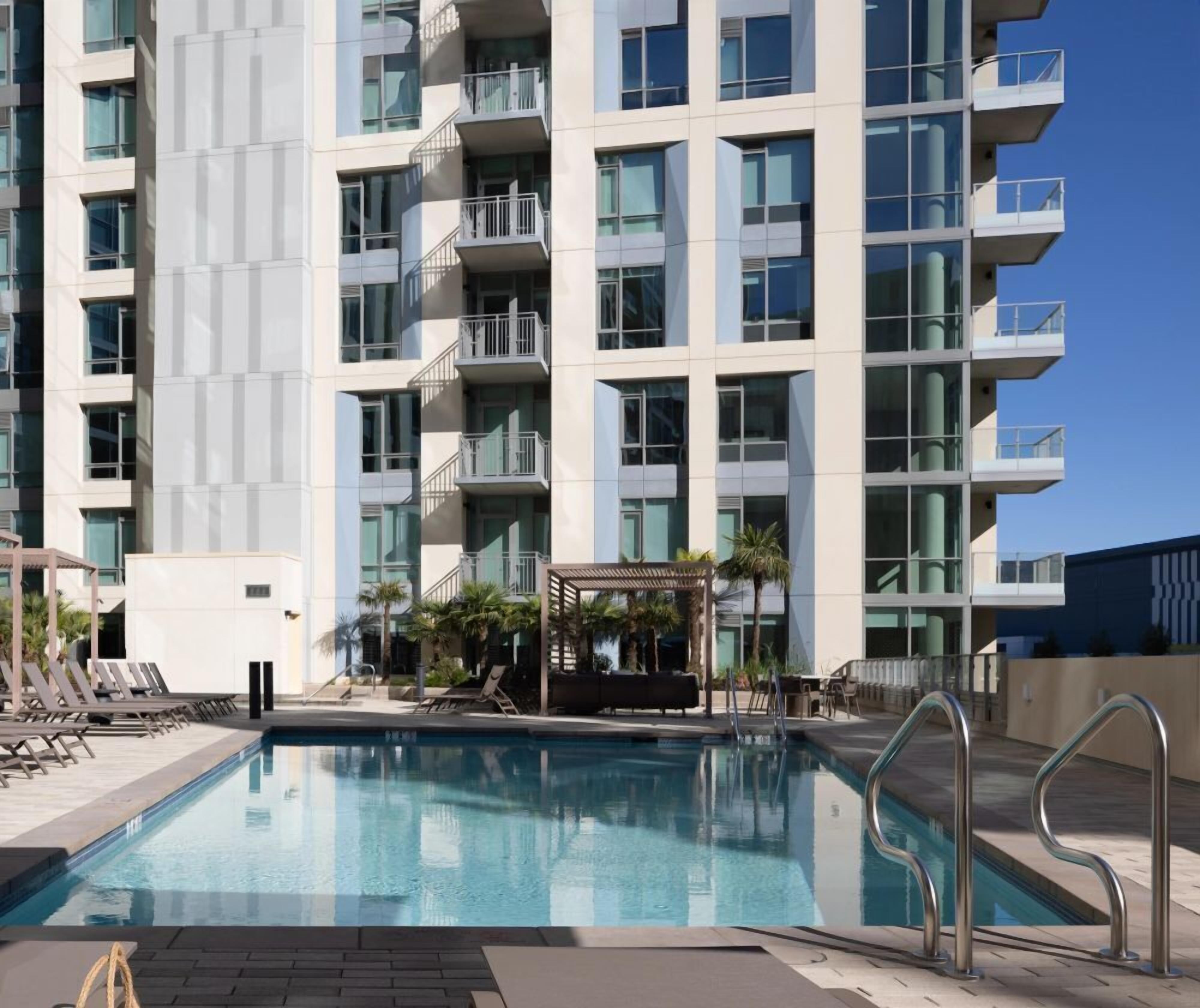 A modern hotel with a swimming pool, multiple balconies, and a covered outdoor seating area.