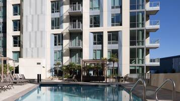 A modern hotel with a swimming pool, multiple balconies, and a covered outdoor seating area.