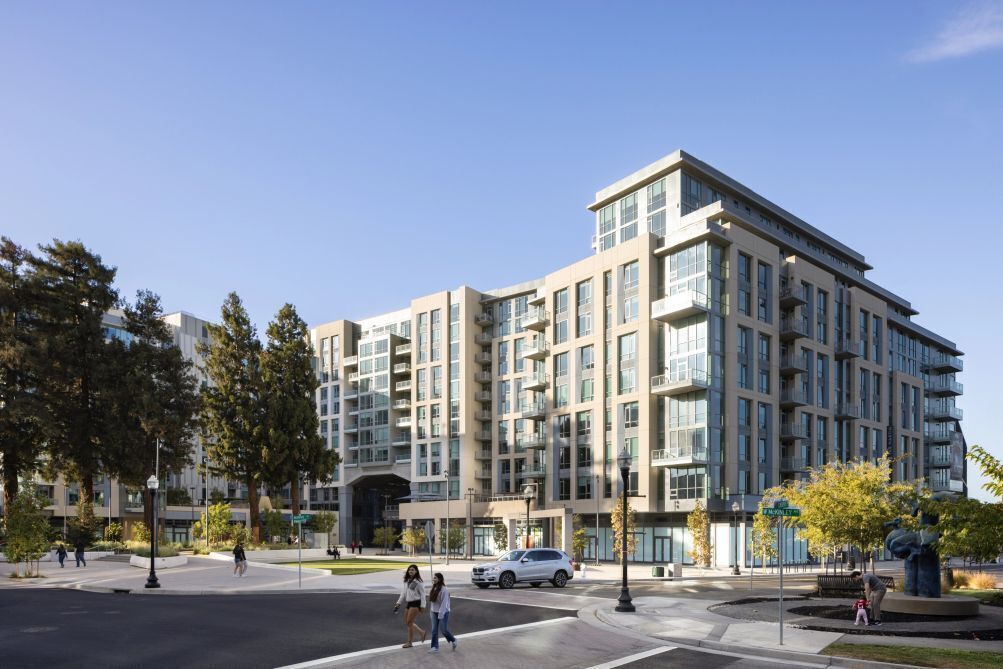 A multi-story building with a modern architectural design, featuring a mix of glass and concrete facades, and a central entrance with a covered area.