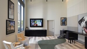 A modern interior with a large TV, artwork on the walls, and a seating area with a green rug. - Spacious 2BR Condo at The Martin with Pool (Sunnyvale)