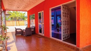 A covered patio area with a wooden floor, a seating arrangement, and a glass door leading to an interior space. - VIST Two-Bedroom Apartment with Pool View unit 1 (Accra)