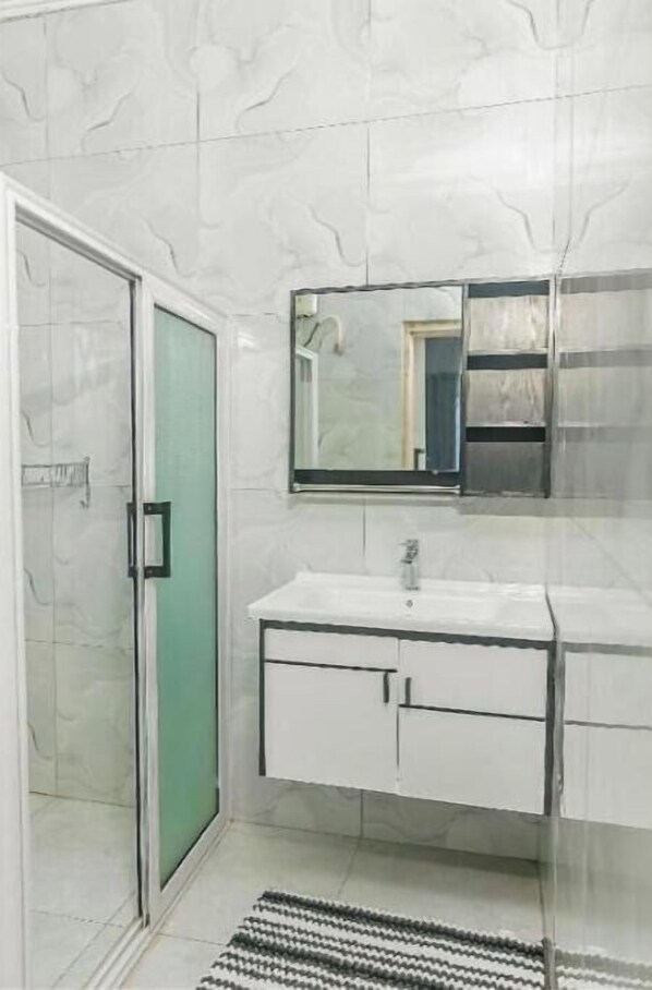 A bathroom with a glass shower door, a white sink with a mirror above it, and a tiled floor.