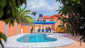 A swimming pool with a tiled deck, surrounded by a covered seating area with blue chairs. - VIST One-Bedroom Apartment with Pool View (Accra)