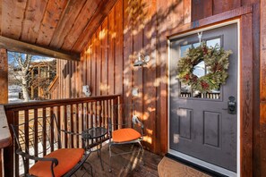 A wooden porch with two chairs and a table, a gray door with a wreath, and a wooden fence in the background. - Updated, Dog Friendly, Fire Pit, Fenced Yard (Crested Butte)