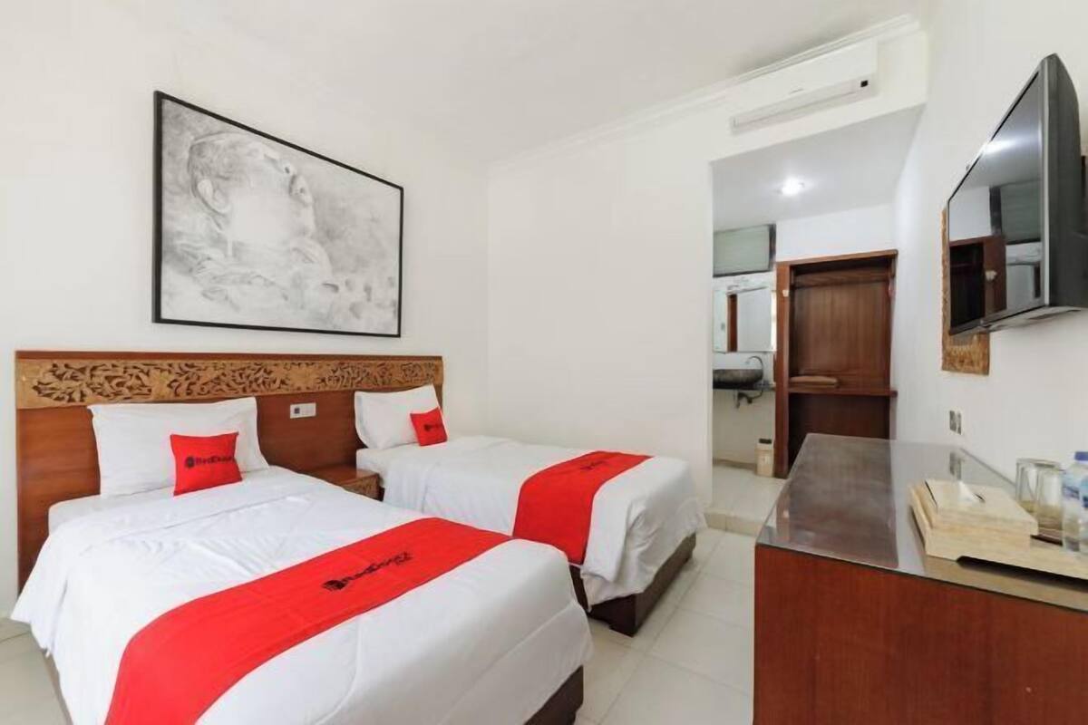 A hotel room with two beds, a wooden headboard, a flat-screen TV, a desk, and a framed picture on the wall.
