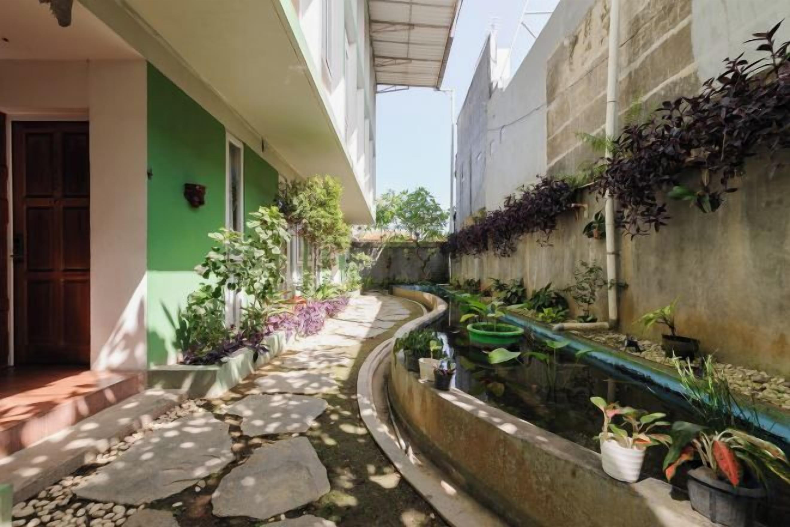 A narrow outdoor corridor with a stone pathway, potted plants, and a water feature.