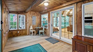 A wooden cabin interior with a dining area, a small table with two chairs, and a large sliding glass door leading to a balcony.