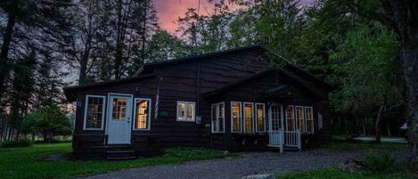 A rustic cabin with a porch, large windows, and an American flag.
