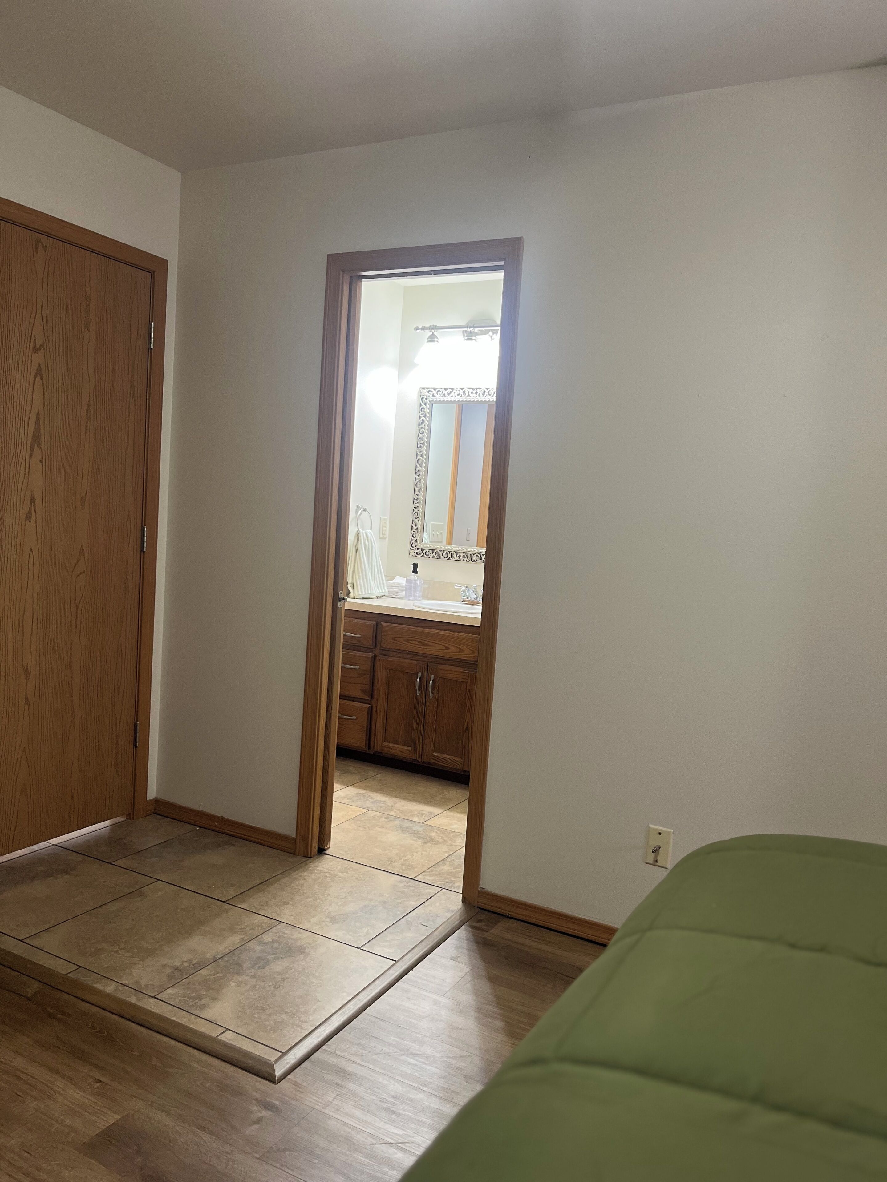 A room with a wooden door, a green bed, and a tiled floor.
