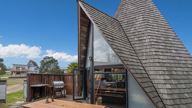 A modern house with a sloped roof, a patio with a wooden table and benches, and a visible kitchen area.