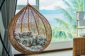 A wicker hanging chair with floral cushions by a window overlooking a tropical landscape. - Puerto Galera Seaview Resort (Puerto Galera)