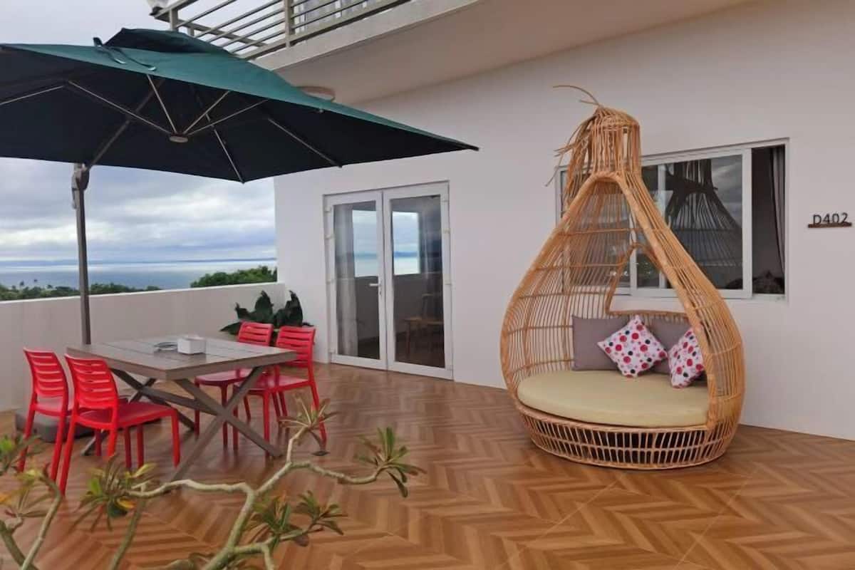 A balcony with a table and chairs, a wicker hanging chair, and a view of the sea.