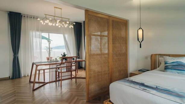 Une chambre d’hôtel avec un lit, une table à manger avec des chaises, un luminaire suspendu et une vue par la fenêtre.