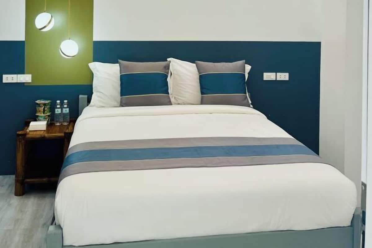 A bed with a striped bedspread, a bedside table with a lamp, and a wall with a circular light fixture.