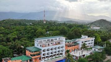 A multi-story building with a swimming pool, surrounded by lush greenery and mountains.