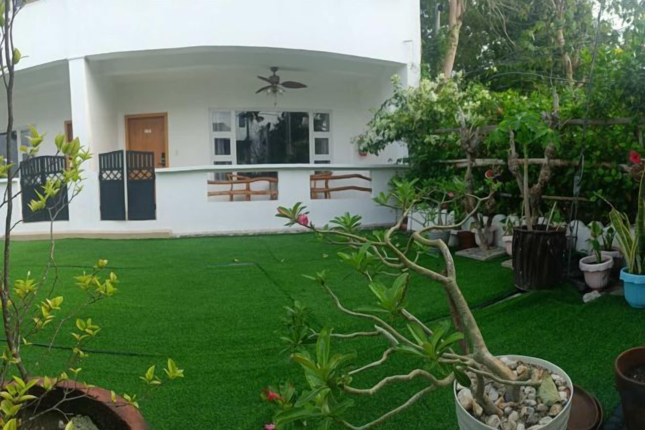 A white building with a curved roof, a door, and windows. There is a green lawn in front, and several potted plants.