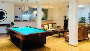 Una mesa de billar en una habitación con piso de espiga, un sofá y una escalera al fondo.