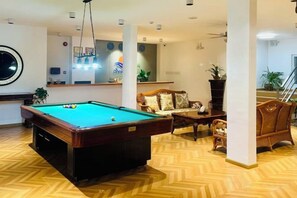 A billiards table in a room with a herringbone floor pattern, a sofa, and a staircase in the background. - Puerto Galera Seaview Resort (Puerto Galera)