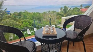 Un balcon avec une table et des chaises, une vue sur la mer et de la verdure.