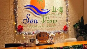 Un espace d’accueil avec une enseigne indiquant « Sea View Resort Philippines », orné d’un palmier et de vagues océaniques.