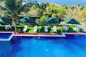 A swimming pool with lounge chairs and umbrellas, surrounded by greenery and a view of the ocean.