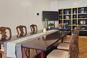 A dining area with a long table, chairs, a plant, a flat-screen TV, and a shelf with decorative items. - Puerto Galera Seaview Resort (Puerto Galera)