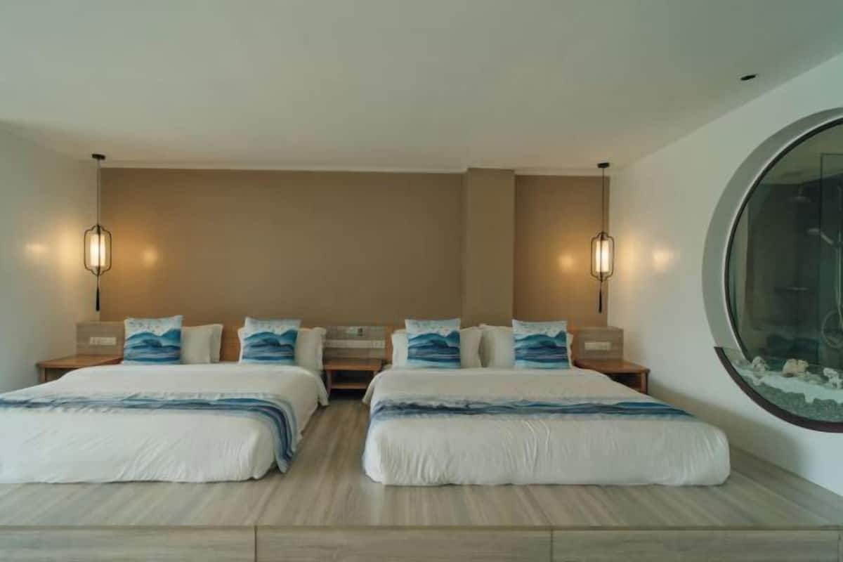 A double room with two beds, nightstands, wall-mounted lamps, and a large circular window.