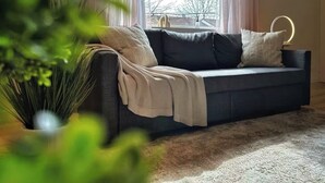 A modern living room with a dark grey sofa, a beige throw blanket, and a round table with a light fixture.