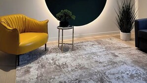 A modern room with a large circular wall feature, a yellow sofa, a small table with a plant, and a tall potted plant.