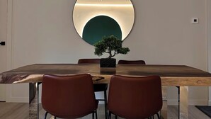 A dining area with a wooden table, four chairs, a round mirror, and a bonsai tree.