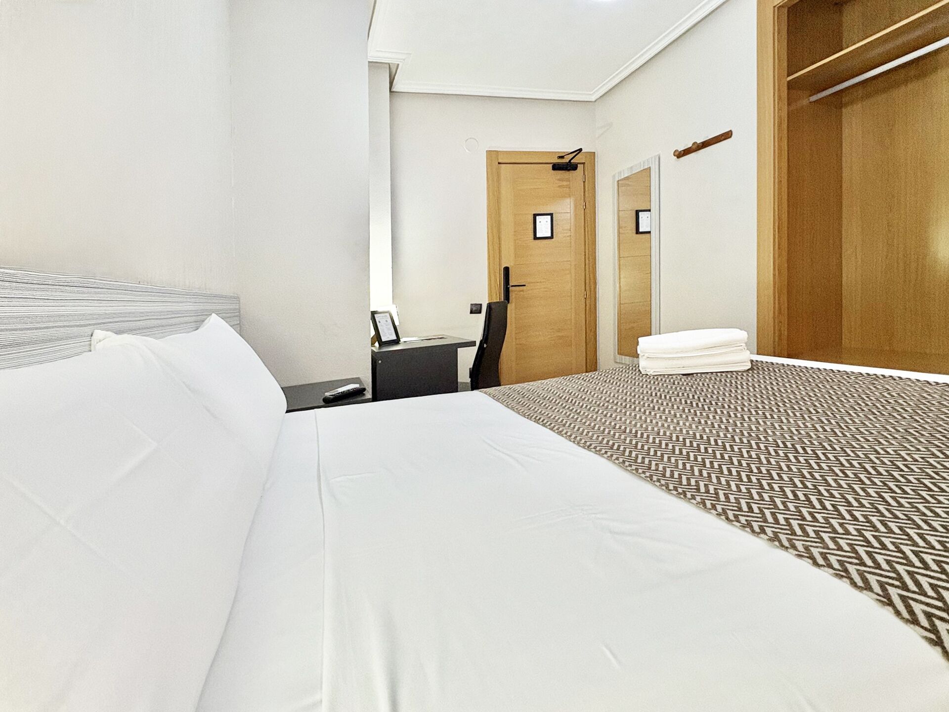Una habitación de hotel con una cama grande, un escritorio, una silla, un armario y un espejo.