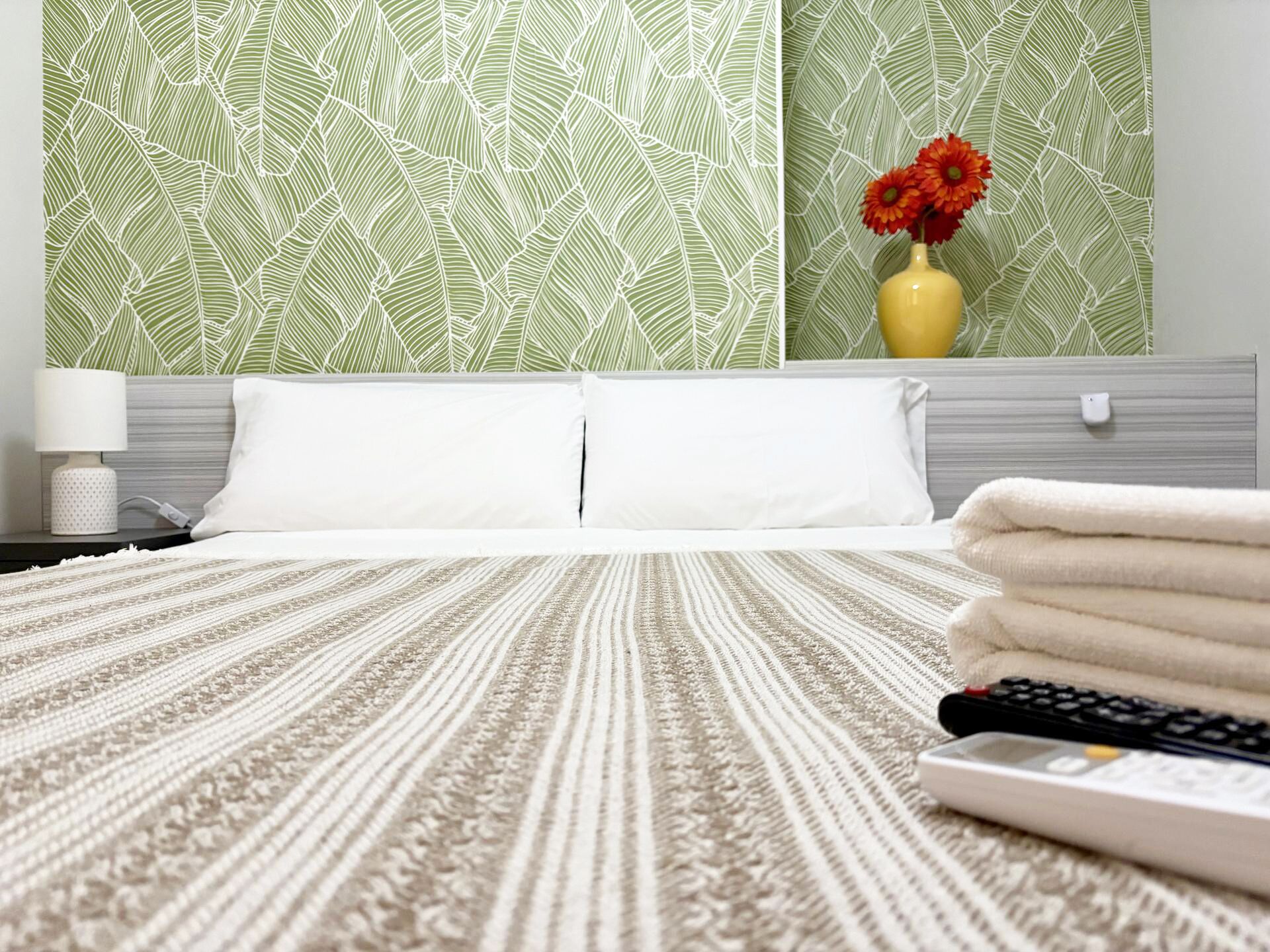 A hotel room with a bed, a remote control, and a vase with flowers on the nightstand.