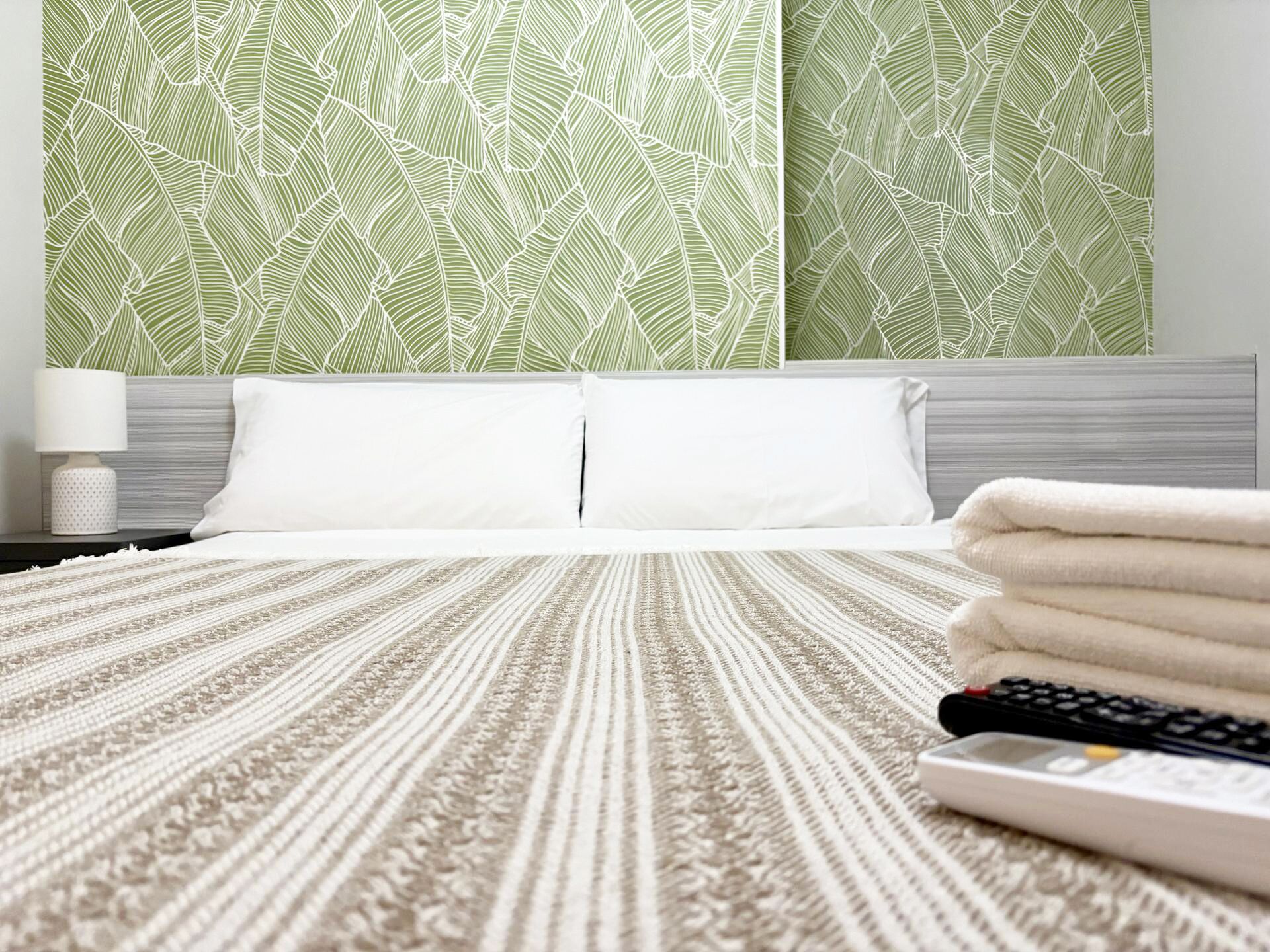 Una habitación de hotel con cama, almohadas, un control remoto y una pared con diseño.