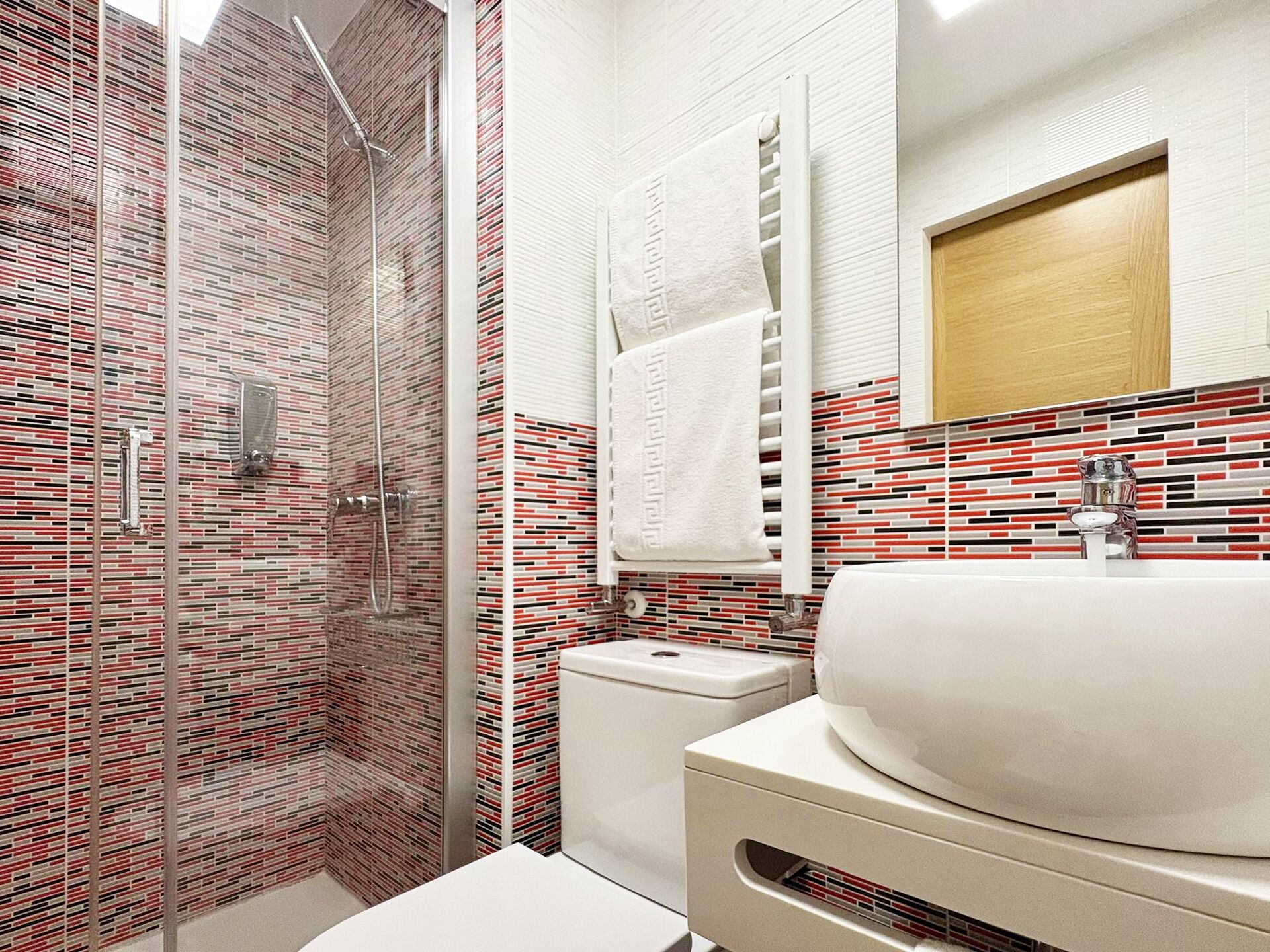 Un baño moderno con ducha de vidrio, lavamanos blanco y salpicadero de azulejos.