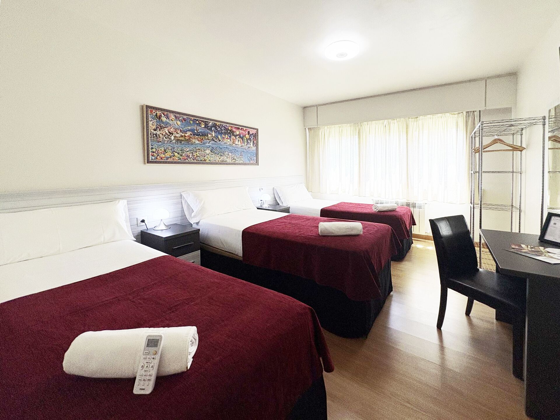 Habitación de hotel con dos camas individuales, un escritorio con silla, un teléfono y un cuadro en la pared.