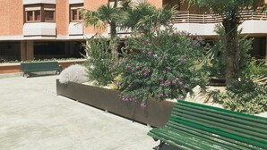A courtyard with a green bench, a planter with flowering plants, and a building with brick and white exterior walls. - Berceo Rooms Self Check-in (Logroño)