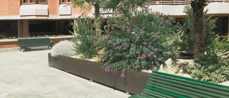 Un patio con un banco verde, una jardinera con plantas florecientes y un edificio con paredes exteriores de ladrillo y blanco.