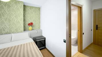 A bedroom with a bed, bedside table, and a mirror. A bathroom is visible through an open door.