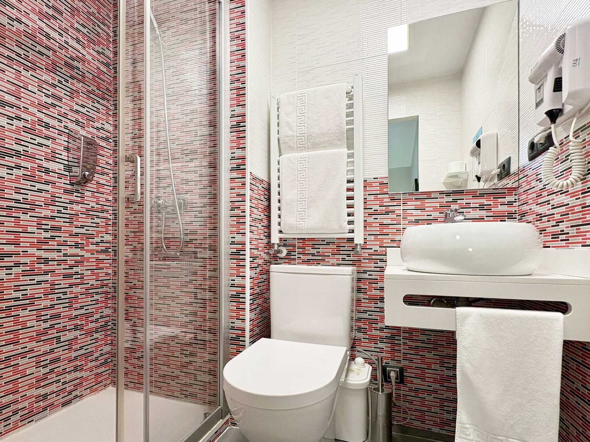 A modern bathroom with a glass shower enclosure, a white toilet, and a sink with a towel rack.