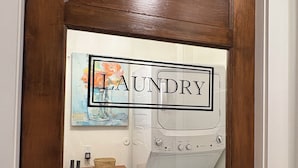 Een houten deur met een spiegel die een wasruimte weerspiegelt, inclusief een wasmachine en een mand.