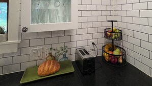 Een keuken met witte betegelde wanden, een vitrinekast, een broodrooster en een fruitmand.