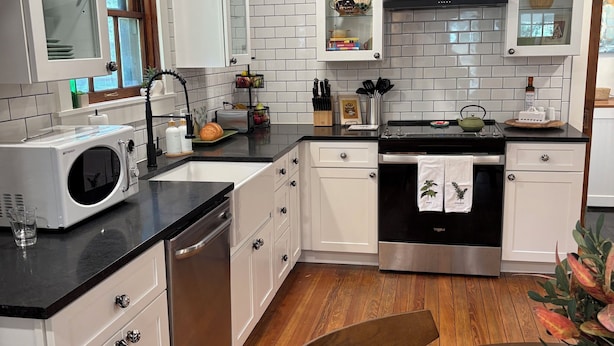 Een moderne keuken met witte kasten, een zwart aanrecht en een houten vloer.
